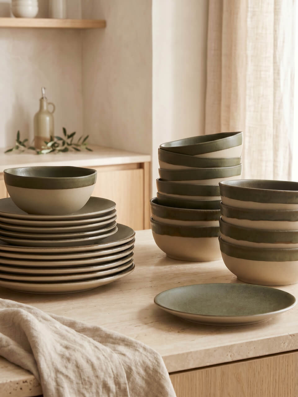 Set of green ceramic bowls and plates on a wooden surface with neutral background