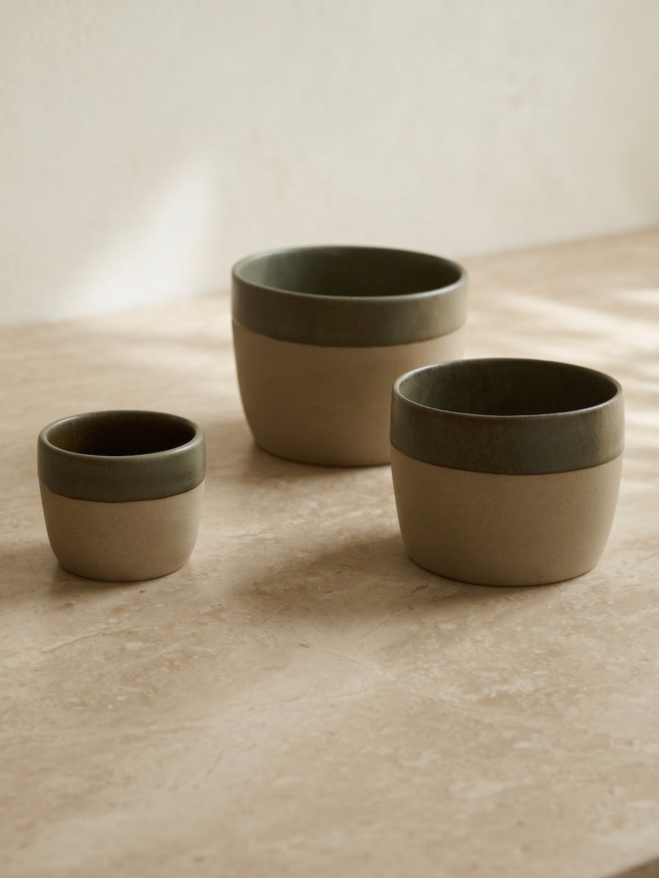 Three ceramic pots with green and beige design on a wooden surface