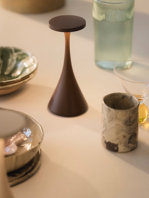Bora corten rechargeable lamp on a white tablecloth with glasses and crockery