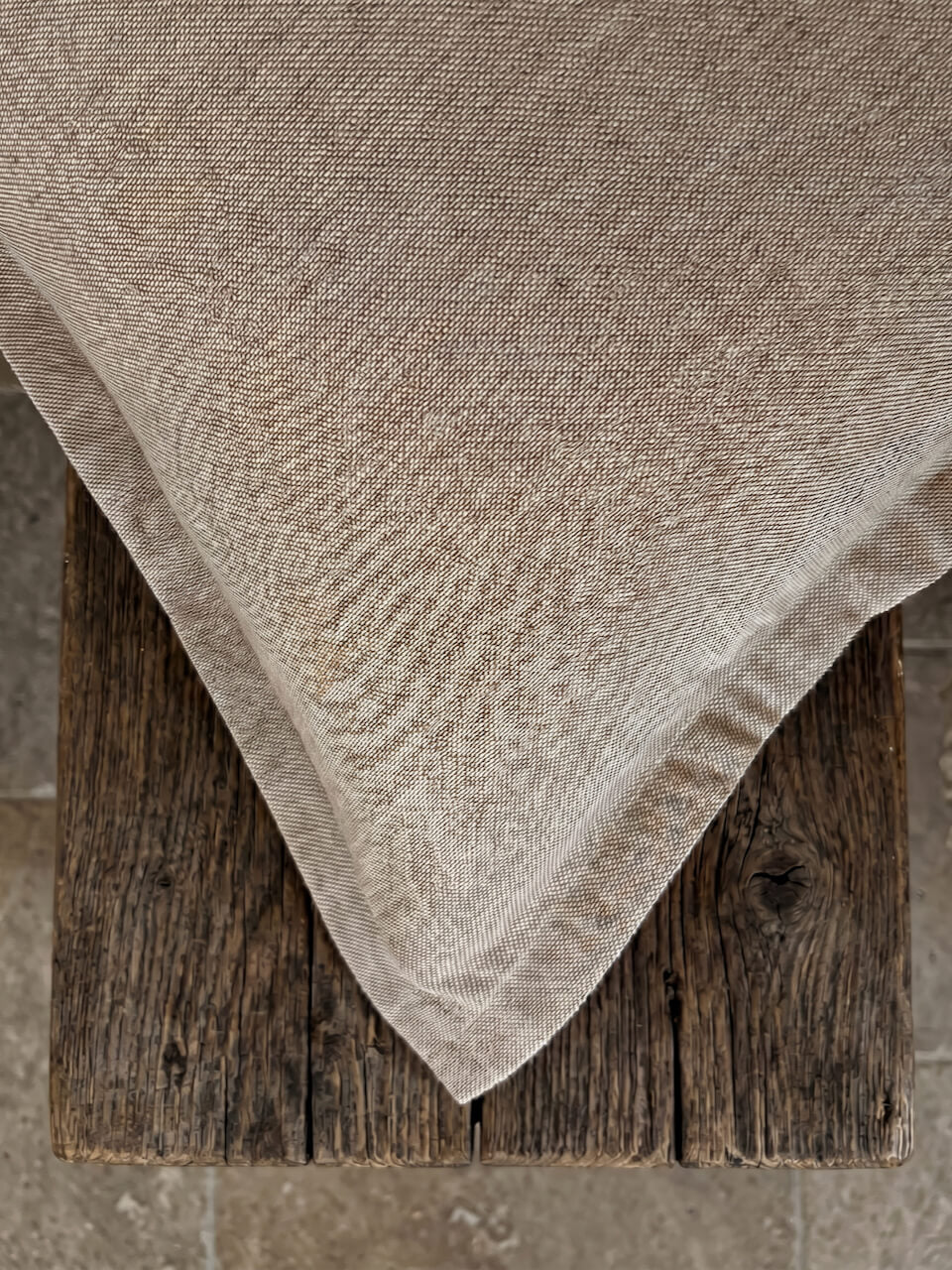 Close-up detail of a luxury caramel cotton linen cushion cover with a soft woven texture and tailored edging, styled on rustic timber for a warm contemporary aesthetic.