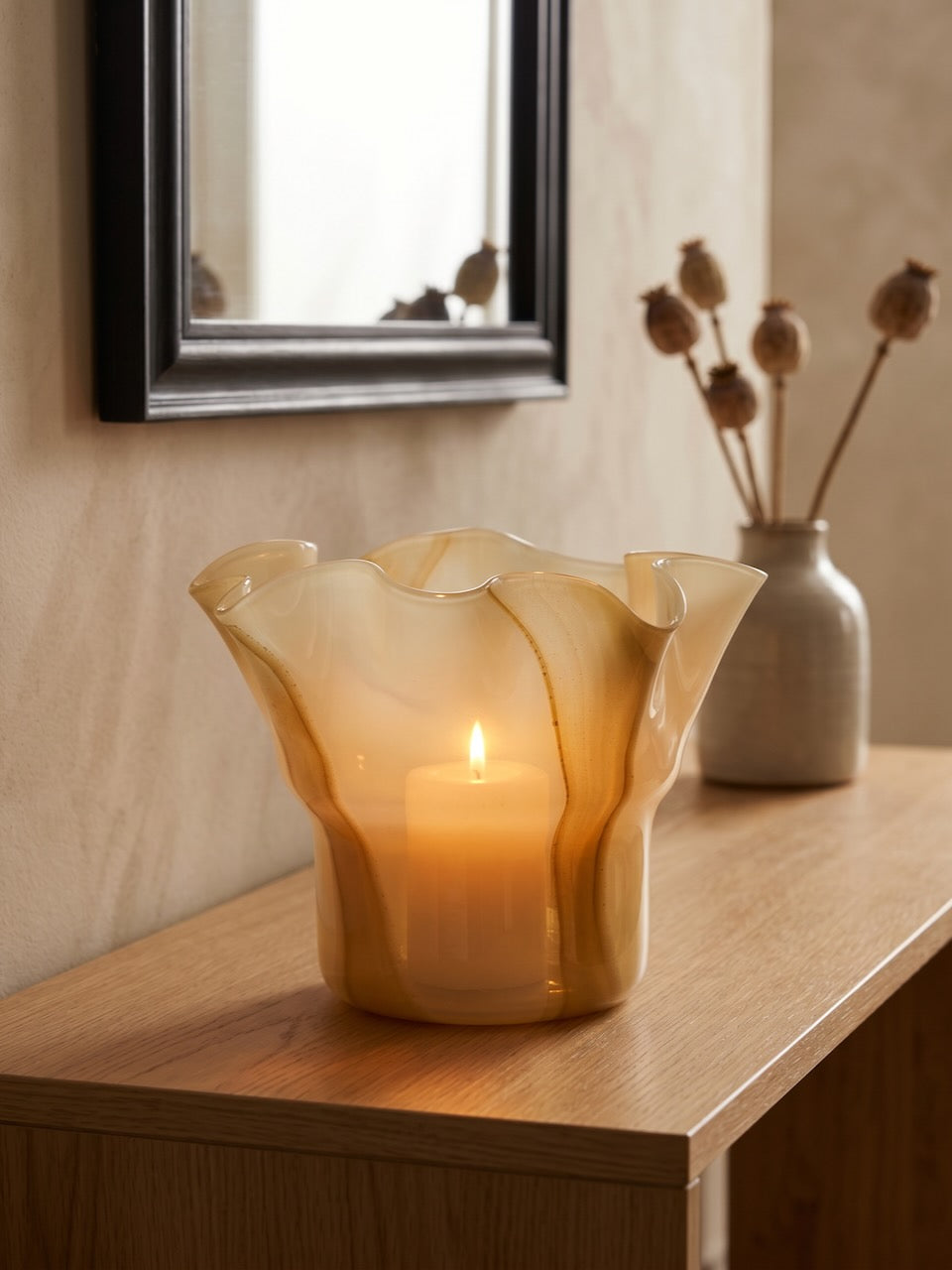 Decorative candle holder on a wooden surface with a mirror and vase in the background.