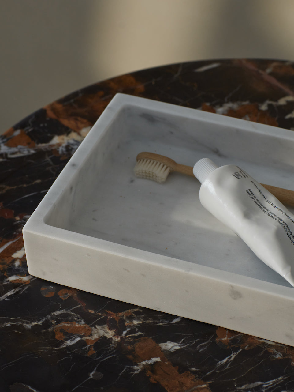 A close up of the Carrara white marble tray showing the soft grey veins running through it on a portoro brown marble side Table