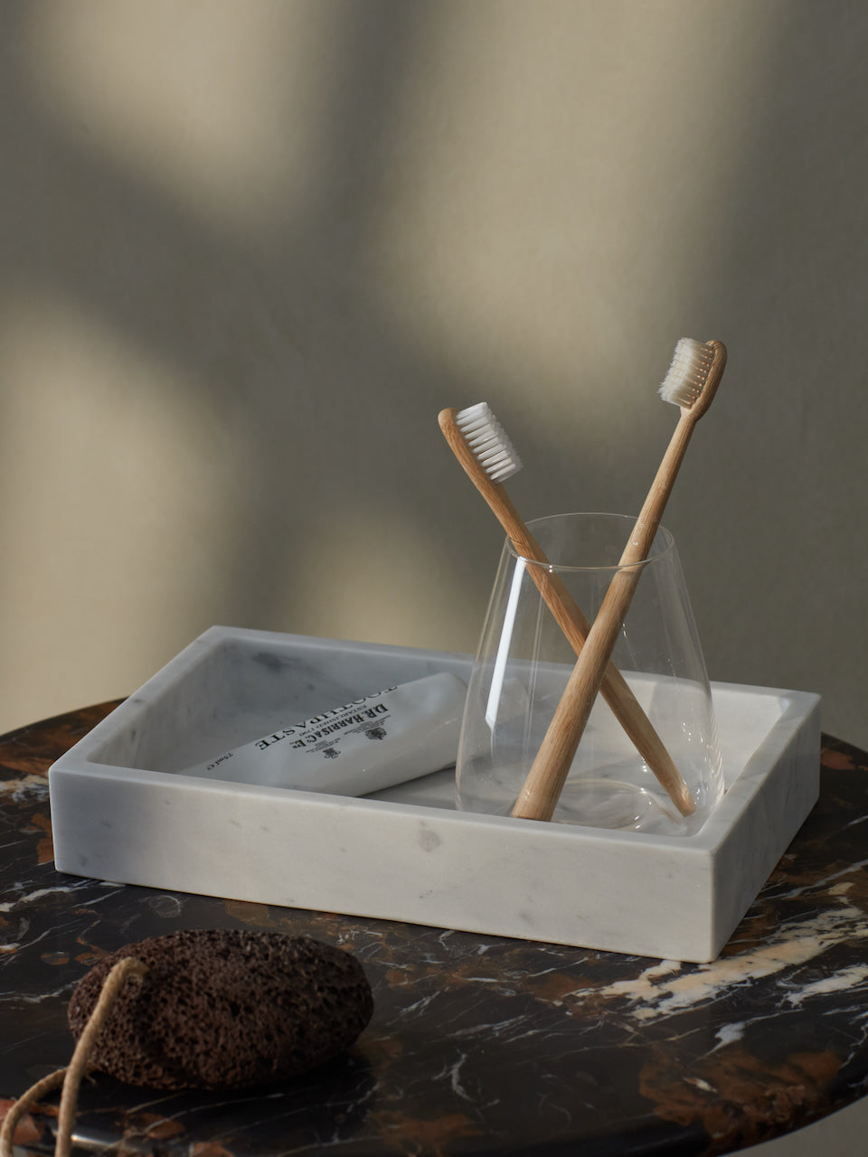 A rectangular Carrara marble tray with a soft grey vein, displayed on a bathroom counter with toothbrushes and a glass cup.