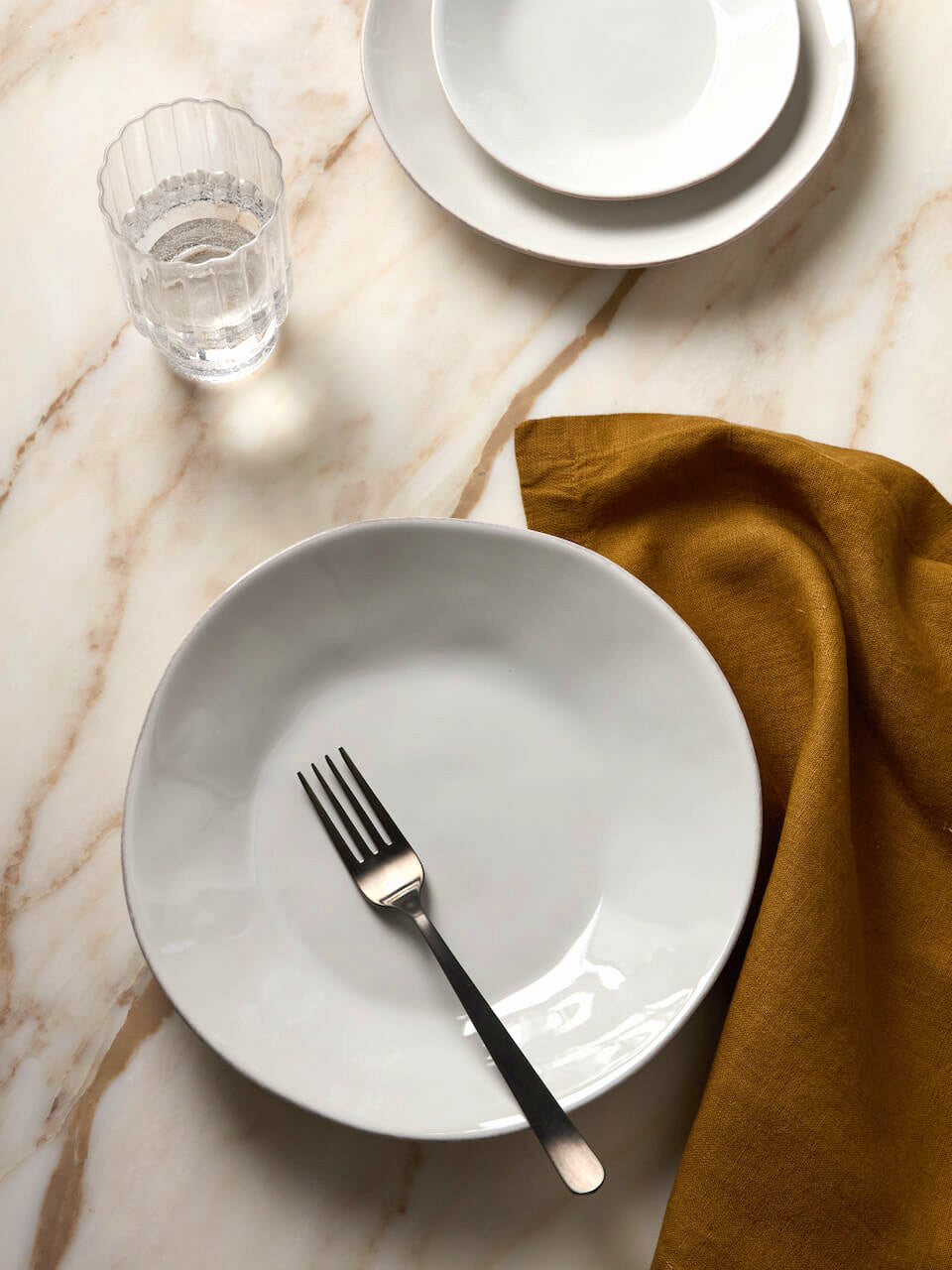White ceramic plate with a fork on a marble surface with a yellow napkin.