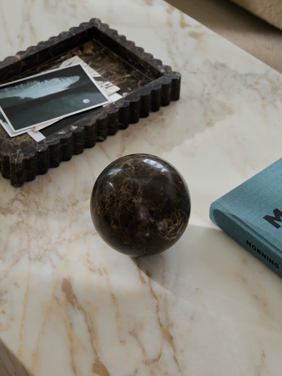 Decorative sphere, brown marble tray with photos, and blue book on a marble surface