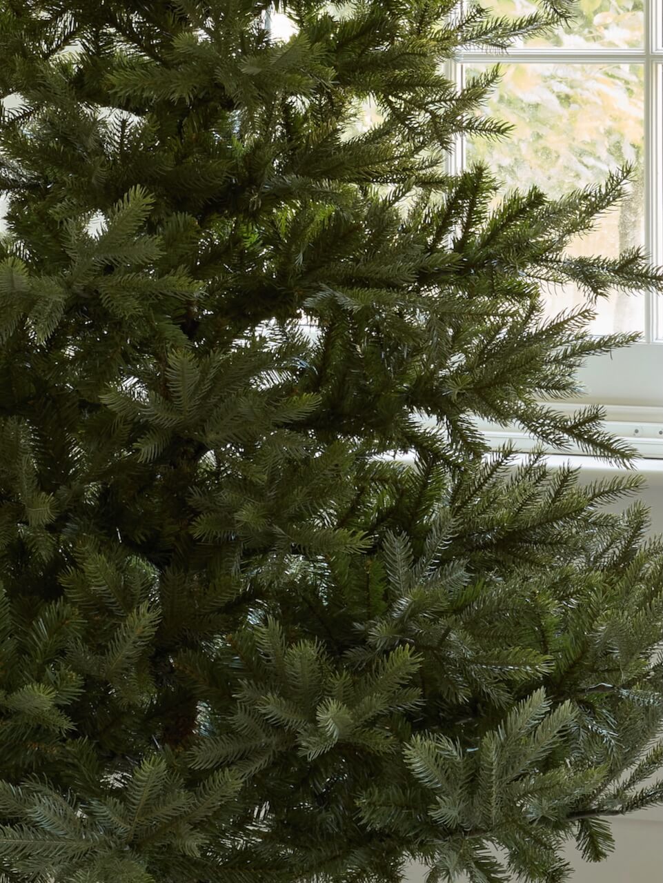 Green artificial Christmas tree against a window with natural light