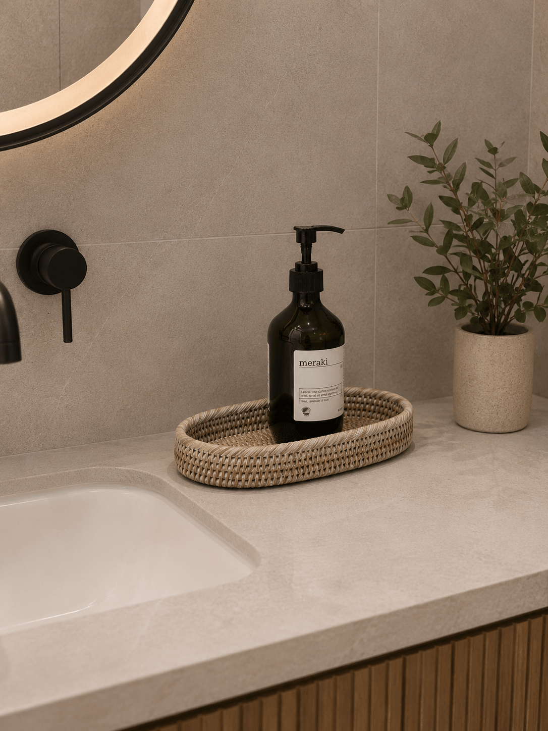 Jarra White rattan bathroom tray styled on a beige stone vanity with a dark amber soap dispenser, black tapware, and a small potted plant for a warm, minimalist look.