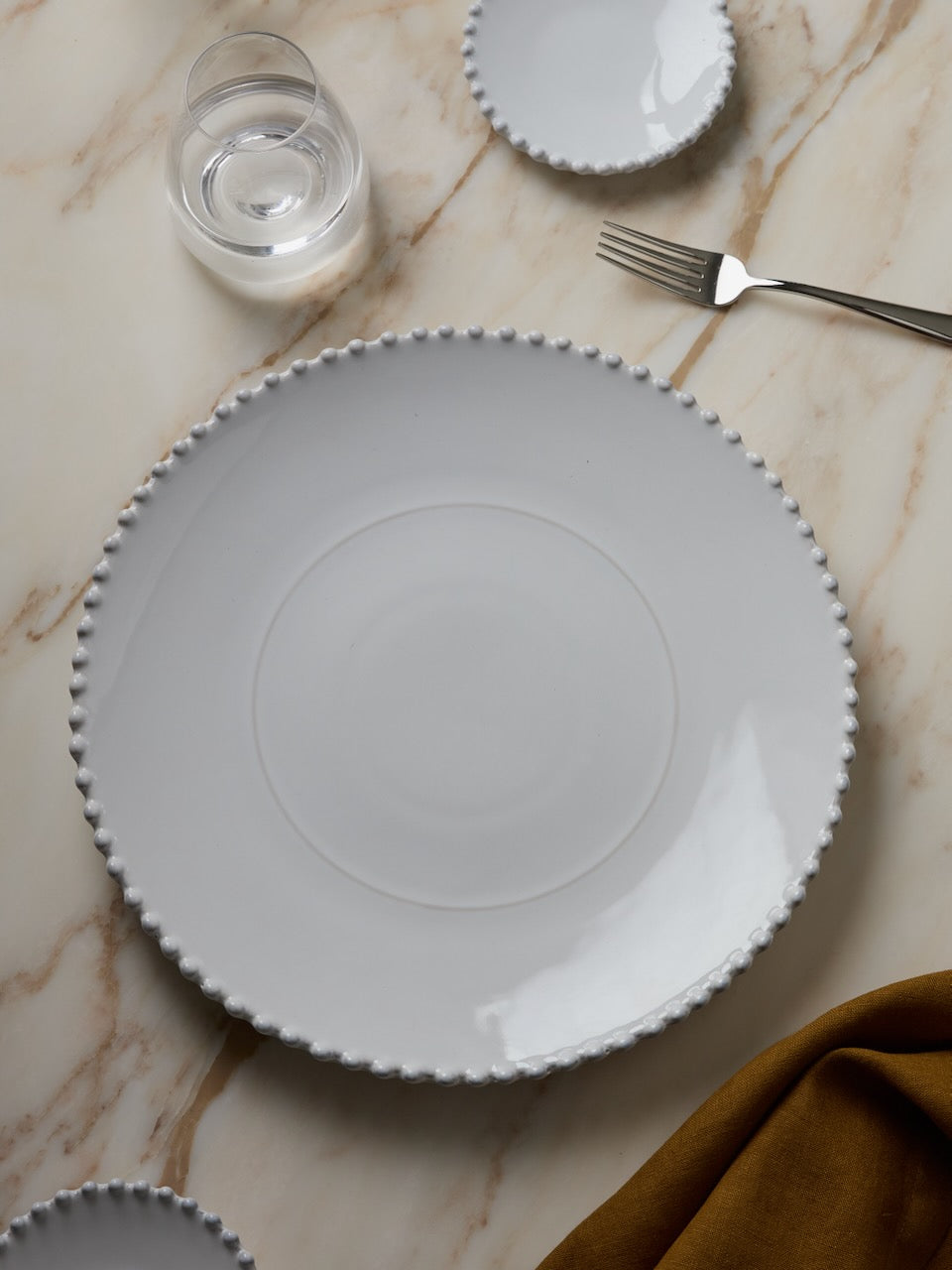 White Pearl ceramic plate with decorative rim on a marble surface with a glass of water and fork.