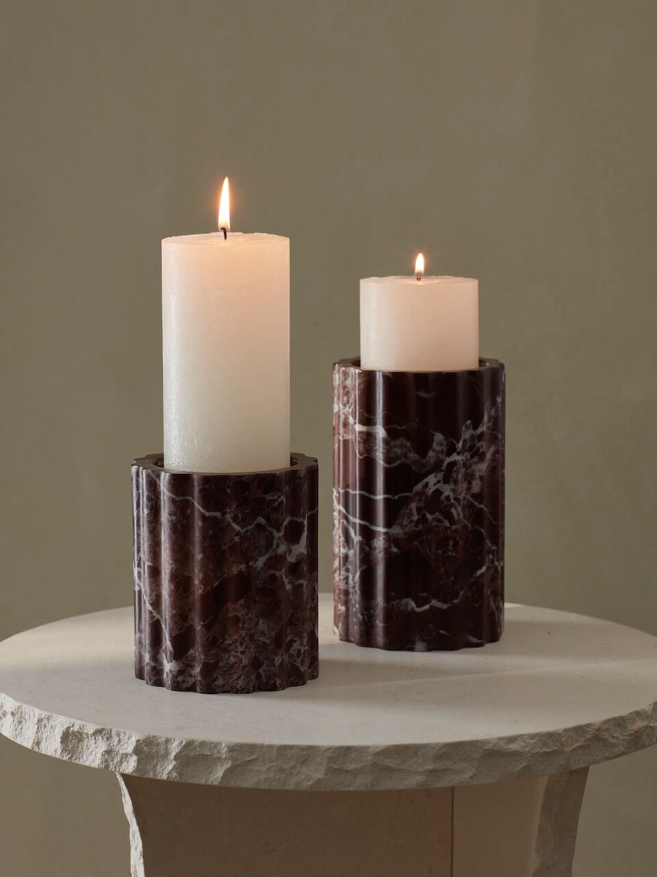 Two cylindrical ribbed burgundy marble candle holders with lit candles on top, placed on a white surface.