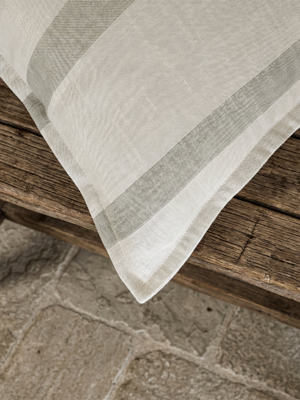 Close-up detail of a luxury sage green striped cotton linen cushion cover featuring soft woven texture and tailored edging, styled on rustic timber for a relaxed contemporary aesthetic.