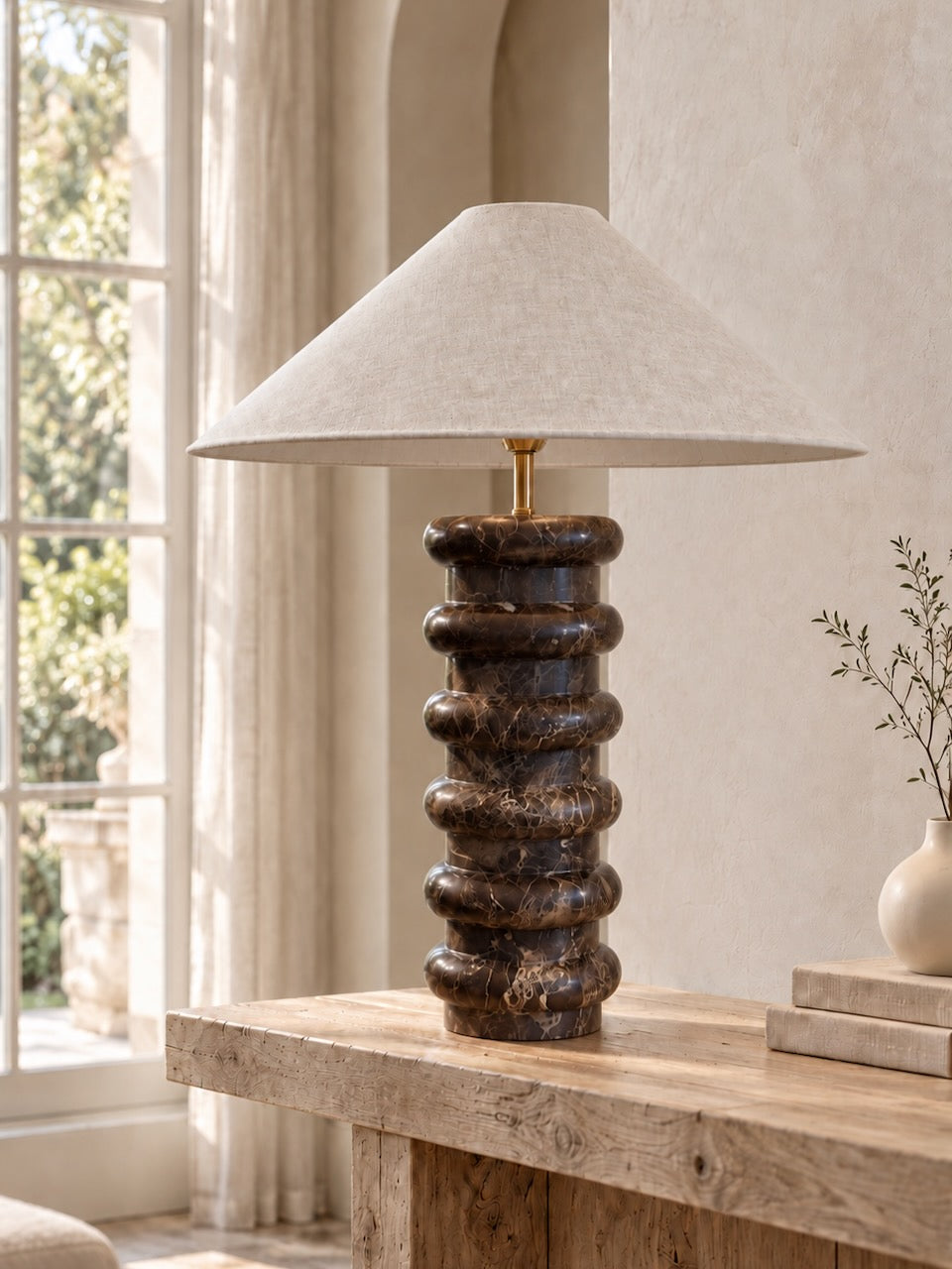A marble table lamp with a textured beige fabric drum shade and a dark brown marble stone base, styled on a rustic wooden table in a warm, neutral-toned room.