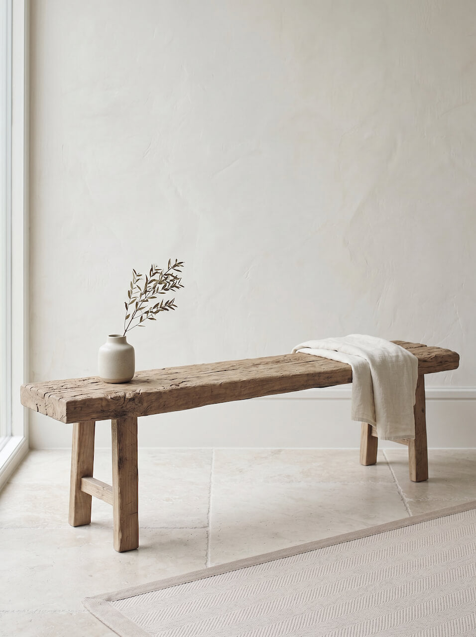 Wooden bench with a vase and plant against a white wall