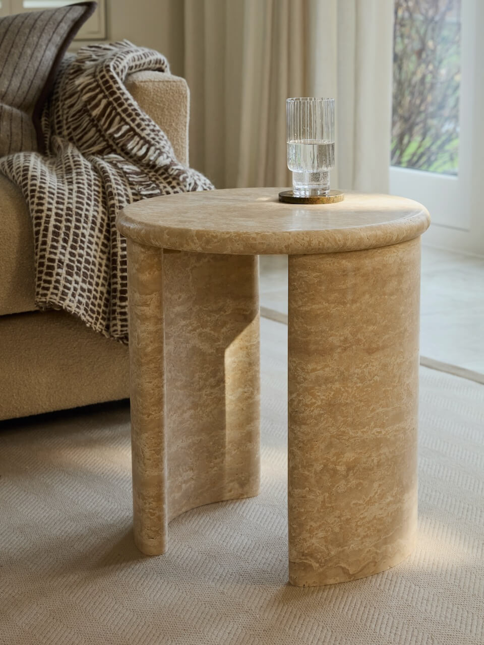 Round stone side table in a living room setting with a lamp on top