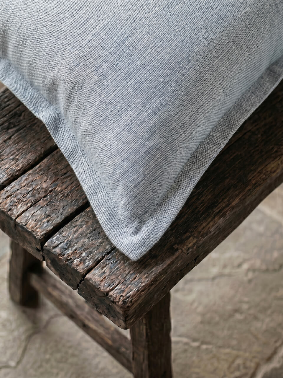 Close-up detail of a luxury blue fog cotton linen cushion cover featuring a soft woven texture and tailored edging, styled on rustic timber for a relaxed contemporary aesthetic.