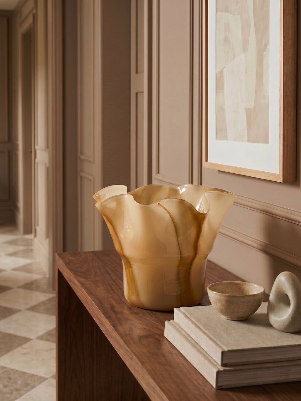 Decorative vase on a wooden shelf in a room with abstract art on the wall.