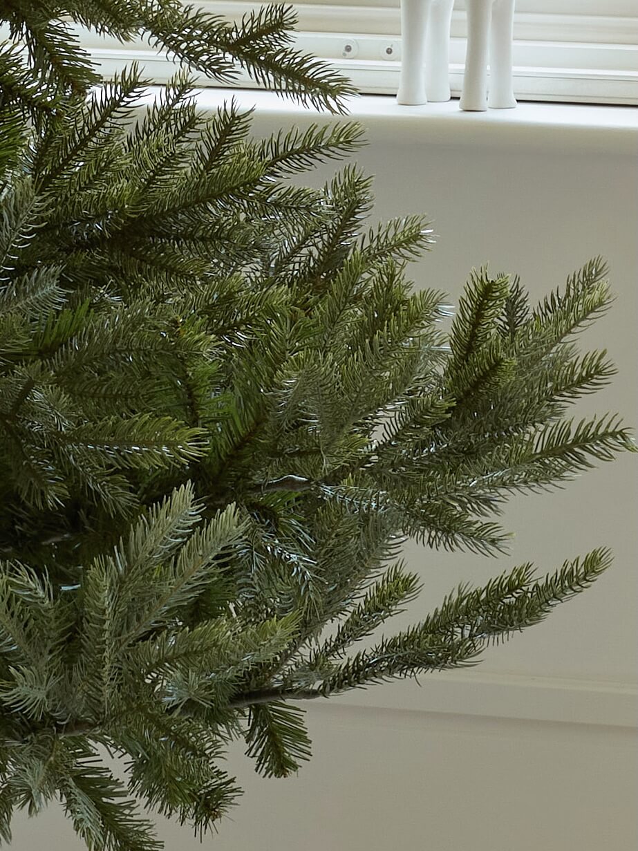 Close-up of a green artificial Christmas tree against a neutral background