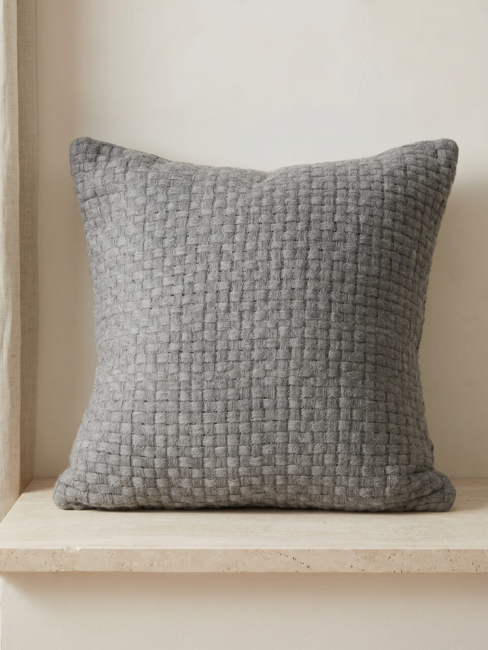 Textured gray pillow on a wooden shelf against a beige wall