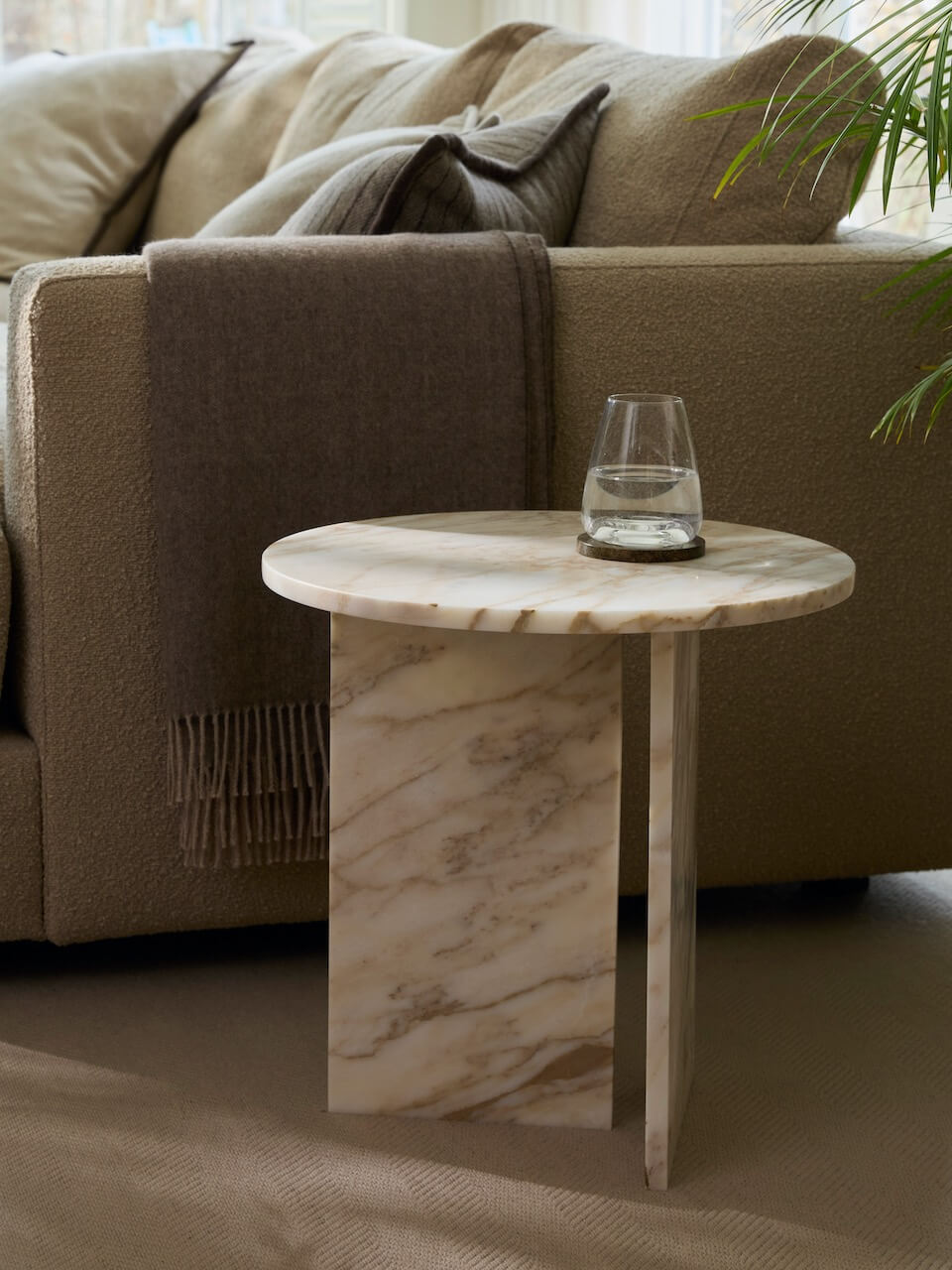 Marble side table with a glass of water in front of a beige sofa.