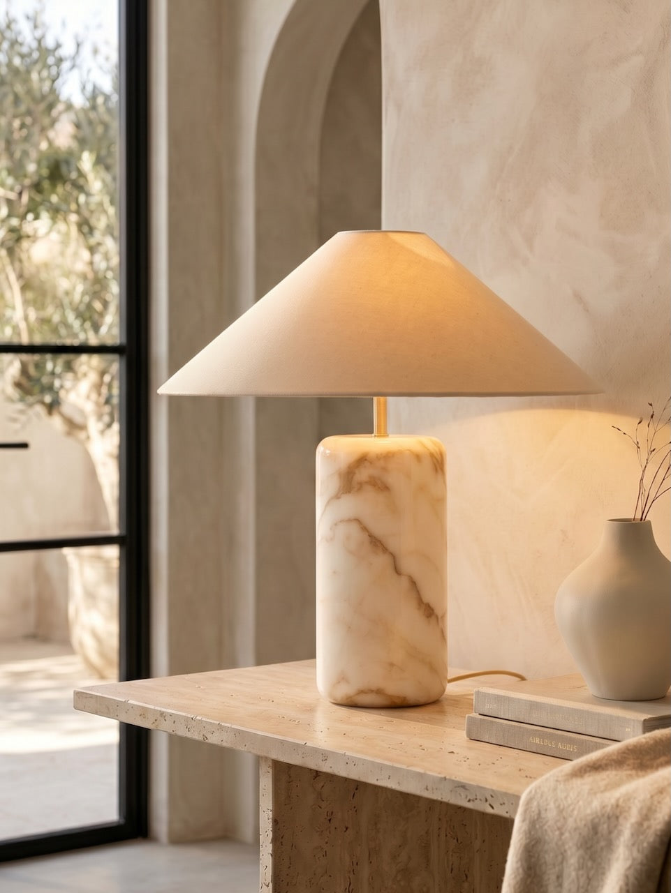 Table lamp with marble base on a wooden table in a room with large windows.
